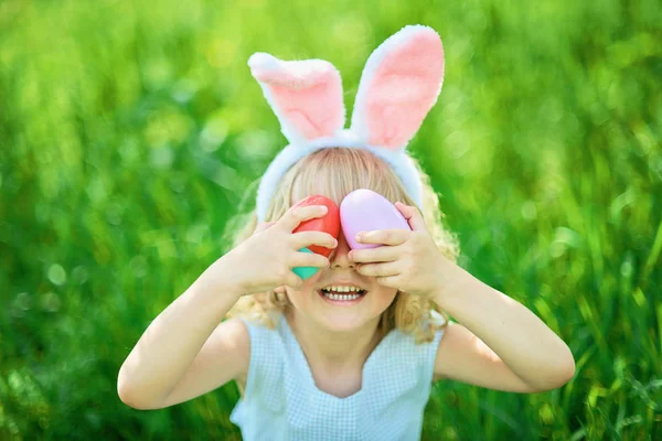 庭でイースターエッグとウサギの耳を持つかわいい面白い女の子 イースターコンセプト イースターエッグハントで笑う子供 卵がいっぱいのバスケット 春のコンセプトの公園の子供 — ストック写真