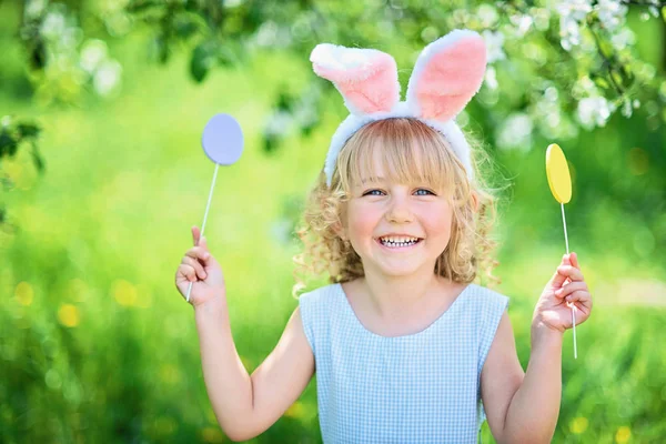 Paskalya yumurtaları ve bahçesinde tavşan kulakları olan sevimli, komik bir kız. Paskalya konsepti. Paskalya yumurtası avında gülen çocuk. Sepet dolusu yumurta ve bahar konseptiyle parkta bir çocuk.