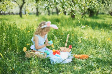 Paskalya yumurtaları ve bahçesinde tavşan kulakları olan sevimli, komik bir kız. Paskalya konsepti. Paskalya yumurtası avında gülen çocuk. Sepet dolusu yumurta ve bahar konseptiyle parkta bir çocuk.
