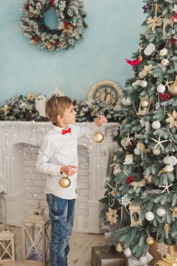 Noel ağacı evde dekorasyon çocuk. Çocuk Noel topları ağaç üzerinde asılı. Noel arifesi kavramı. gülümseyen yakışıklı çocuk Noel ağacının yanında duruyor.