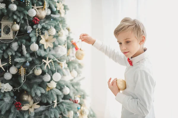 Child decorating Christmas tree at home. Boy hangs Christmas balls on tree. Christmas Eve concept. smiling handsome boy stands near a Christmas tree.