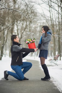 Romantik Fırsat evlenmek. adam sevgilisini kış park için bir teklif yapar. Sevgililer günü teklif kavramı. Çiçek boquet kız için valentineday içinde veren genç adam.