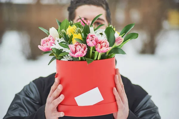 man holding red gift box with beautiful bouquet of blooming flowers, romantic moment, woman day and Valentines Day. delivery courier man delivering box with flowers. Copy space