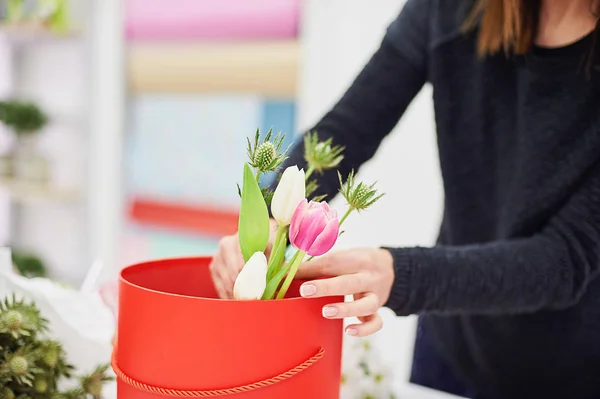 Close-up hands of florist with flowers. Florist holding blooming bouquet of pink tulips on a linen background. Flowershop concept.