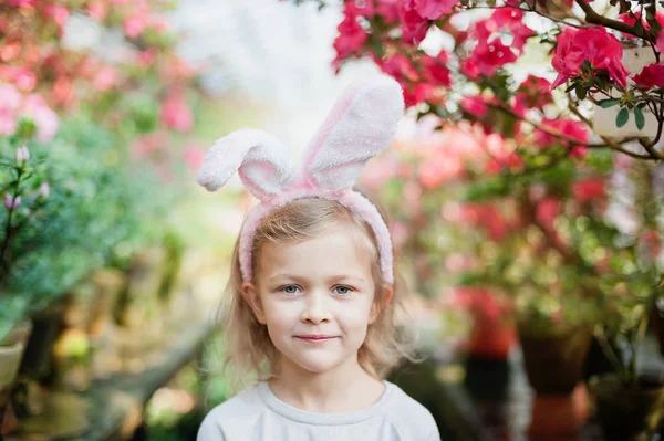 Милая забавная девушка с пасхальными кроличьими ушами в саду. Пасхальная концепция. Смеющийся ребенок во время охоты за пасхальными яйцами . — стоковое фото