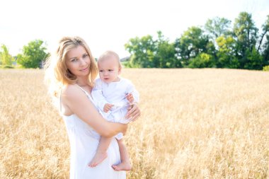 Anne ve kızı buğday tarlasında. Mutlu Aile açık havada. Sağlıklı bir çocuk, annesi ile piknikte altın mısır gevreği tarlasında ekmek ve sütle..