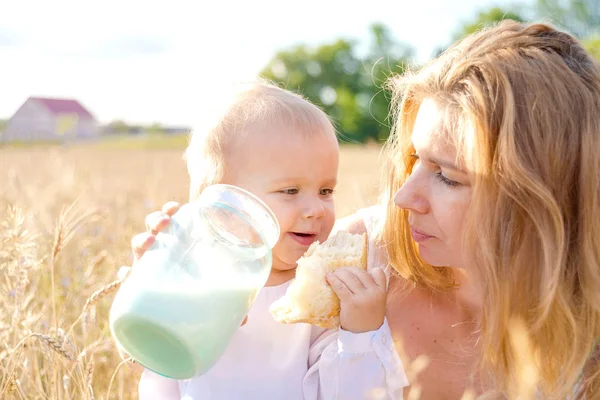 Madre e hija en el campo de trigo. Familia feliz al aire libre. niño sano con madre en el picnic con pan y leche en el campo de cereales de oro . — Foto de Stock