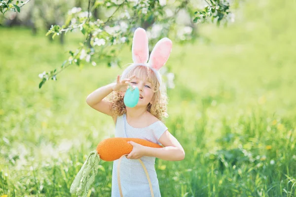 Мила смішна дівчина з великодніми яйцями і вухами кролика в саду. Великодня концепція. Сміється дитина на полюванні на великодні яйця — стокове фото