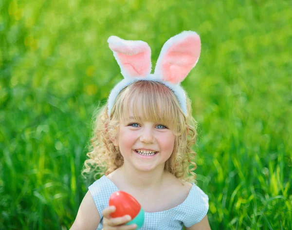 Мила смішна дівчина з великодніми яйцями і вухами кролика в саду. Великодня концепція. Сміється дитина на полюванні на великодні яйця — стокове фото