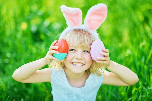 Cute zabawna dziewczyna z pisanki i uszy króliczka w ogrodzie. koncepcji Wielkanocnej. Śmiech dziecko w Polowanie na jajka wielkanocne — Zdjęcie stockowe