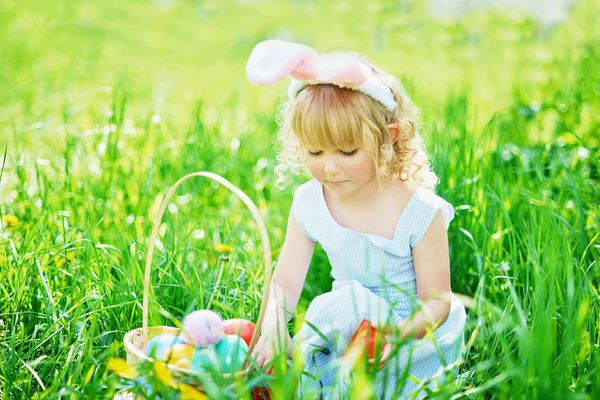 Linda chica divertida con huevos de Pascua y orejas de conejo en el jardín. concepto de Pascua. Riendo niño en la búsqueda de huevos de Pascua — Foto de Stock