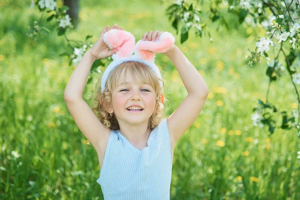 Linda chica divertida con huevos de Pascua y orejas de conejo en el jardín. concepto de Pascua. Riendo niño en la búsqueda de huevos de Pascua —  Fotos de Stock