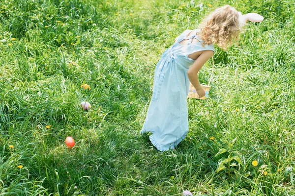 Nettes lustiges Mädchen mit Ostereiern und Hasenohren im Garten. Osterkonzept. Lachendes Kind bei der Ostereiersuche — Stockfoto