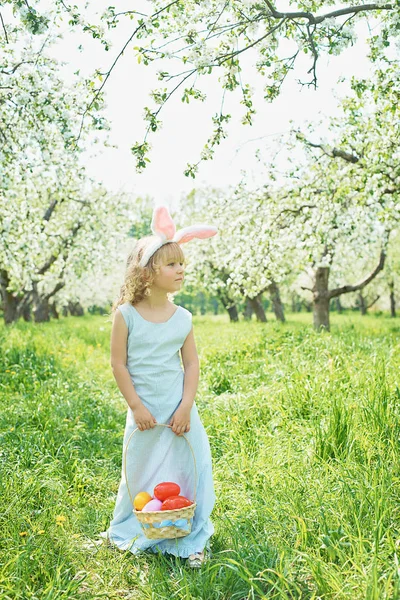 可爱的有趣的女孩与复活节彩蛋和兔子耳朵在花园里。复活节的概念。笑的孩子在复活节彩蛋狩猎 — 图库照片