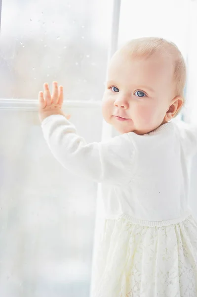 Blondes lockiges Kleinkind Baby Mädchen, das durch ein Fenster schaut. — Stockfoto