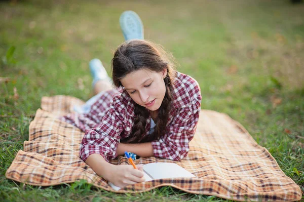 The girl sitting under the tree and wrote in Notepad — Stock Photo, Image