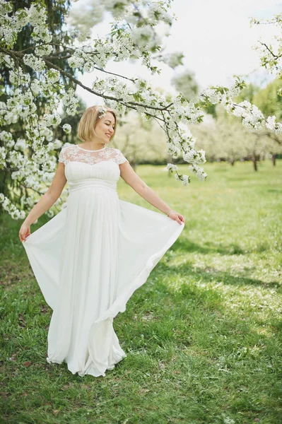 Tavaszi hangulat, szép terhes nő illata virágzás cseresznye fa, élvezve a természet, fehér virágos kert. — Stock Fotó