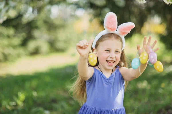 Cute zabawna dziewczyna z pisanki i uszy króliczka w ogrodzie. koncepcji Wielkanocnej. Śmiech dziecko w Polowanie na jajka wielkanocne. — Zdjęcie stockowe