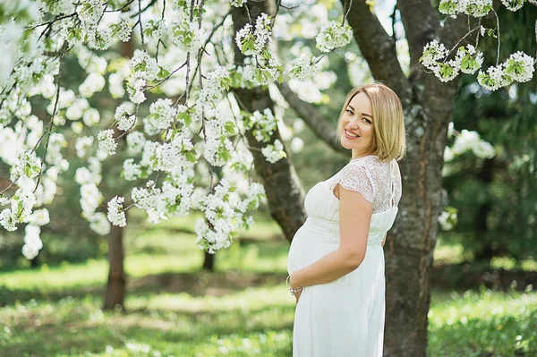 Modo primaverile, bella donna incinta odore di ciliegio in fiore, godersi la natura, bianco giardino floreale . — Foto Stock