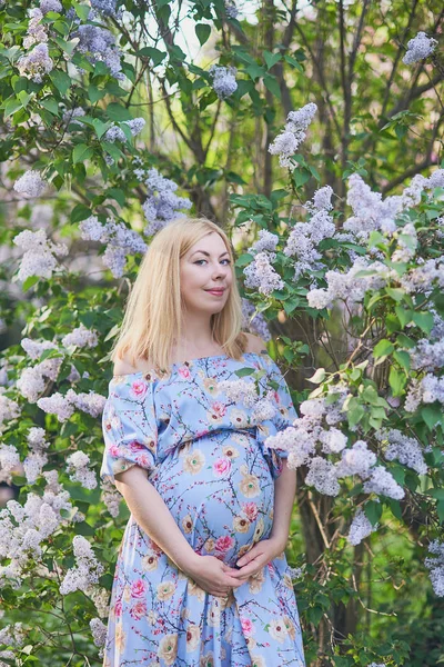 Modo primaverile, bella donna incinta odore albero fiorito, godersi la natura, rosa giardino floreale. futura madre rilassante e godersi la vita nella natura — Foto Stock