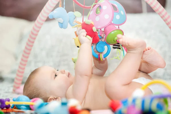 Baby auf einem Teppich liegend. Spielen in mobilen. Lernspielzeug. Süßes Kind krabbelt und spielt mit Spielzeug auf Teppich — Stockfoto