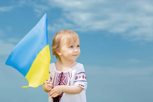 Dziecko nosi trzepoczącą niebiesko-żółtą flagę Ukrainy na polu. Dzień Niepodległości Ukrainy. Dzień Flagi. Dzień Konstytucji. Dziewczyna w tradycyjnym hafcie z flagą Ukrainy. — Zdjęcie stockowe