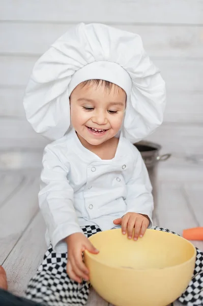 Retrato de medio cuerpo de un pequeño chef. Lindo niño pequeño en delantal y sombrero de chef está mirando a la cámara . — Foto de Stock