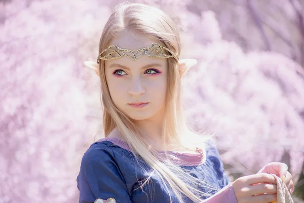 Peri masalı kızı. Gizemli elf kızı portresi. Cosplay karakteri. Çiçek açan bir bahçede elf portresi. Uzun kulaklı bir kız dokunur.