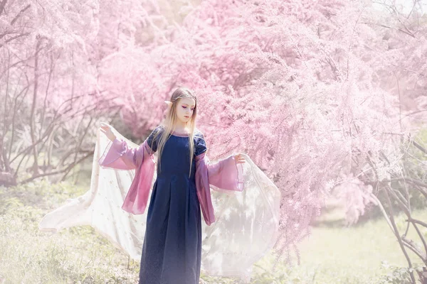 Chica de cuento de hadas. Retrato de una chica elfa mística. Personaje de Cosplay. Retrato de elfo en un jardín floreciente. Una chica con orejas largas toca . —  Fotos de Stock