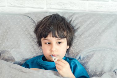 grip hasta çocuk ağızda tıbbi termometre tutan ve evde yatakta yatarken
