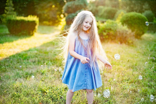 Kind wervelend, dansen speelt op het weitje. Meisje heeft plezier met bubbels. schattig klein lang haar blond meisje dansen met zeepbellen bij zonsondergang park — Stockfoto