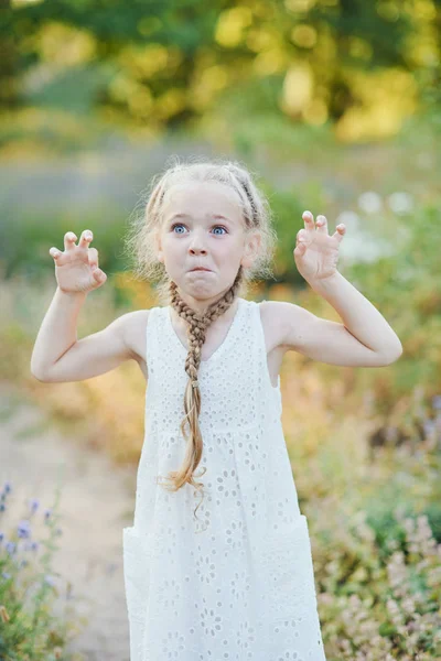 Menina engraçada segurando tranças de cabelo. Menina bonito pequeno com longo cabelo loiro ao ar livre. Miúdo a expressar emoções. Abril tolo . — Fotografia de Stock