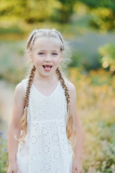 Grappig meisje het houden van haar vleit. Klein schattig meisje met lange blonde haren tonen tong outdoor. Kid uitdrukken van emoties. April Fool. — Stockfoto