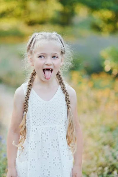 有趣的女孩拿着头发辫子。小可爱的女孩与长金发显示舌头户外。孩子表达情感。愚人节. — 图库照片