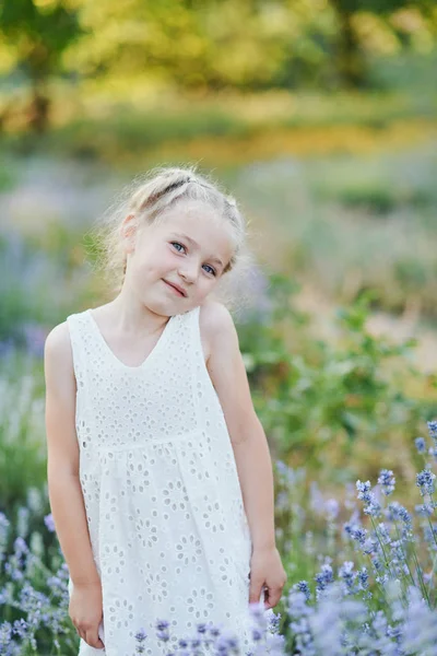 Kis lány levendula területén. gyerekek fantáziáját. Mosolygós lány szippantás virágok nyáron lila levendula mező. — Stock Fotó