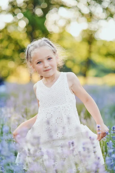 Niña en el campo de lavanda. Fantasía infantil. Chica sonriente oliendo flores en el campo de lavanda púrpura de verano . — Foto de Stock