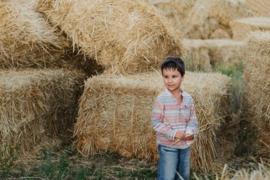 Küçük çocuk çiftlik arazisinde saman balyaları arasında yürüyor