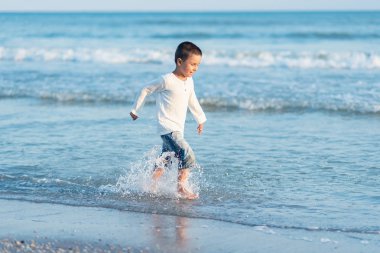Sahilde koşan bir çocuk. Yaz tatili. Mutlu çocuk gün batımında kumsalda oynuyor.