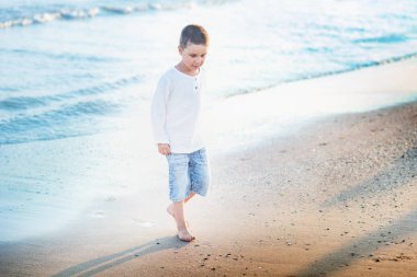 Sahilde koşan bir çocuk. Yaz tatili. Mutlu çocuk gün batımında kumsalda oynuyor.