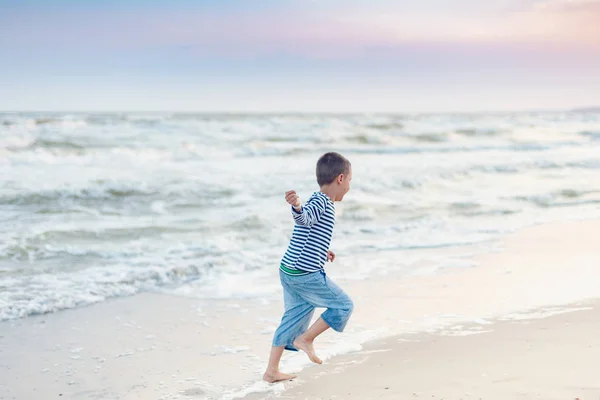 海岸を走っている子供。夏休みだ。幸せな子供は日没時にビーチで遊んでいます — ストック写真