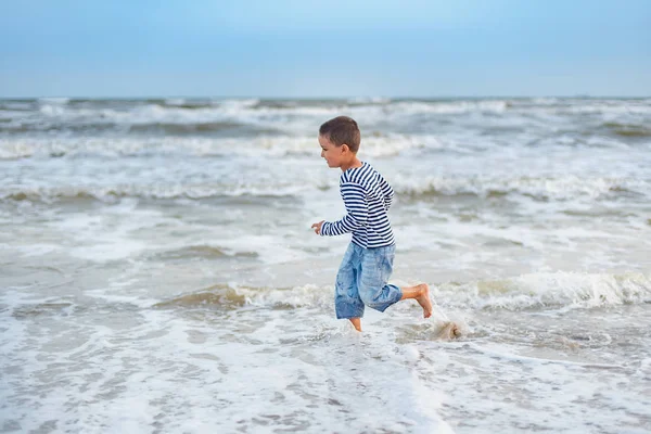 海辺の縞模様のTシャツの少年 海岸を走っている子供 夏休みだ 幸せな子供は日没時にビーチで遊んでいます — ストック写真