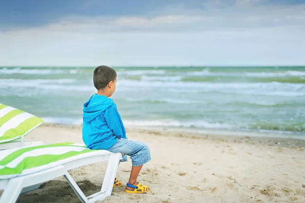 Miúdo triste sozinho sentado na praia, a olhar para o mar e a pensar. No fim do verão. tristeza sobre o fim de férias . — Fotografia de Stock