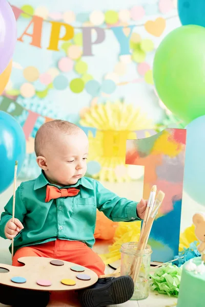 男孩一岁生日的装饰品 以艺术画家的风格粉碎蛋糕 婴儿微笑着看着相机 可爱的高加索男婴坐在演播室木地板上庆祝的肖像 — 图库照片