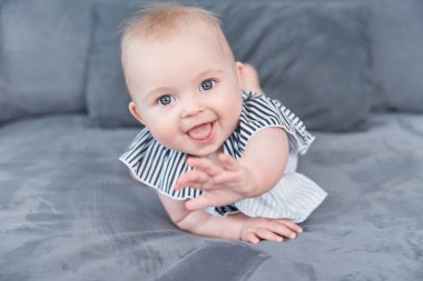 Yatakta gülümseyen tatlı bir kız bebek. Gri yumuşak battaniyeli yedi aylık bir bebek. Sevimli mavi gözlü bebek. Boşluğu kopyala.