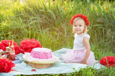 İki yaşında kız yeşil çim kutlama süslemeleri ve Doğum günü pastası yakın oturuyor 
