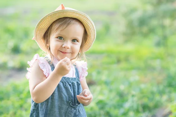 夏の庭でエンドウ豆のポッドを食べる帽子の小さな農家の女の子 子供のコンセプトのための健康的な食事 — ストック写真