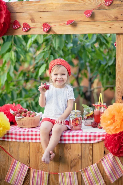 Limonata standında oturan çilek serinletici içecekler ile sevimli küçük kız 