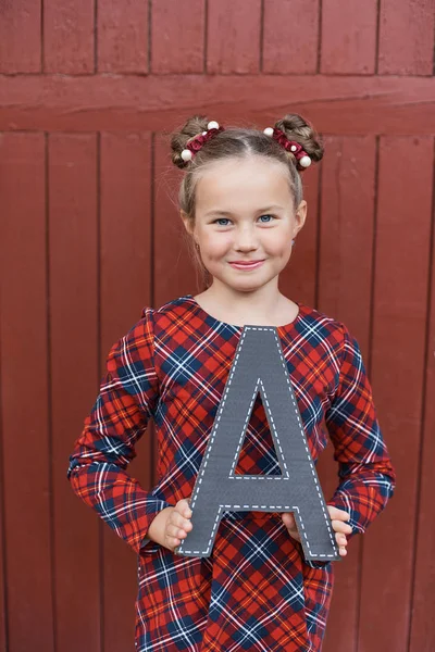 Gelukkig Schoolmeisje Houden Decoratieve Letter Handen Poseren Rode Houten Achtergrond — Stockfoto