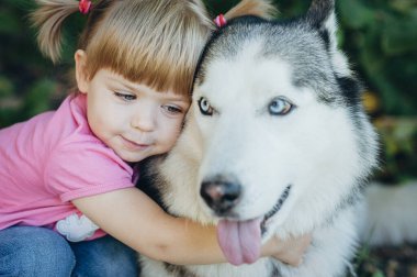 Parkta köpeğe sarılan sevimli küçük kız. Güzel güneşli hava, parlak güneş ışığı ve sevimli modeller. Köpek gibi ağır nefes alıyorsun, pembe dilin sarkıyor.