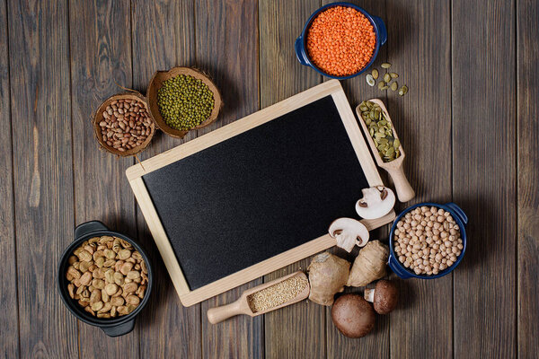 Ноги, чечевица, горох с фасолью вид сверху. Состав различных видов бобовых в чашах на деревянном фоне. Черная доска с копировальным пространством
